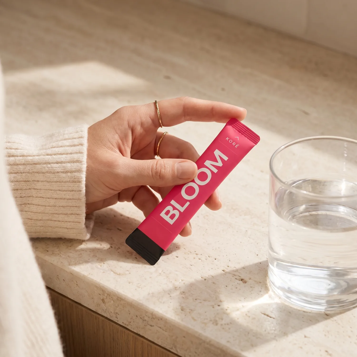 KORÊ BLOOM daily creatine stick pack held at a stone counter in warm morning light