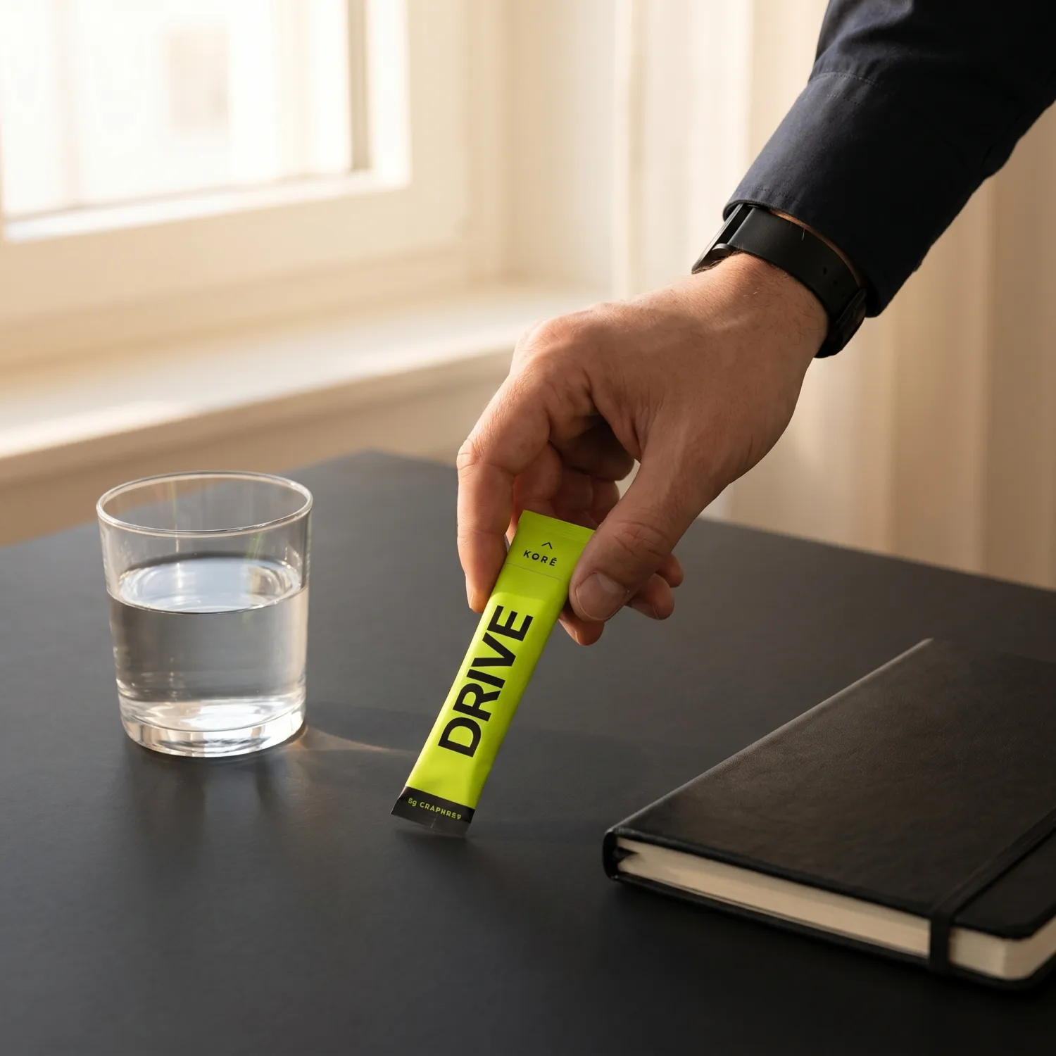 KORÊ DRIVE daily creatine stick pack held at a desk with a glass of water in morning light