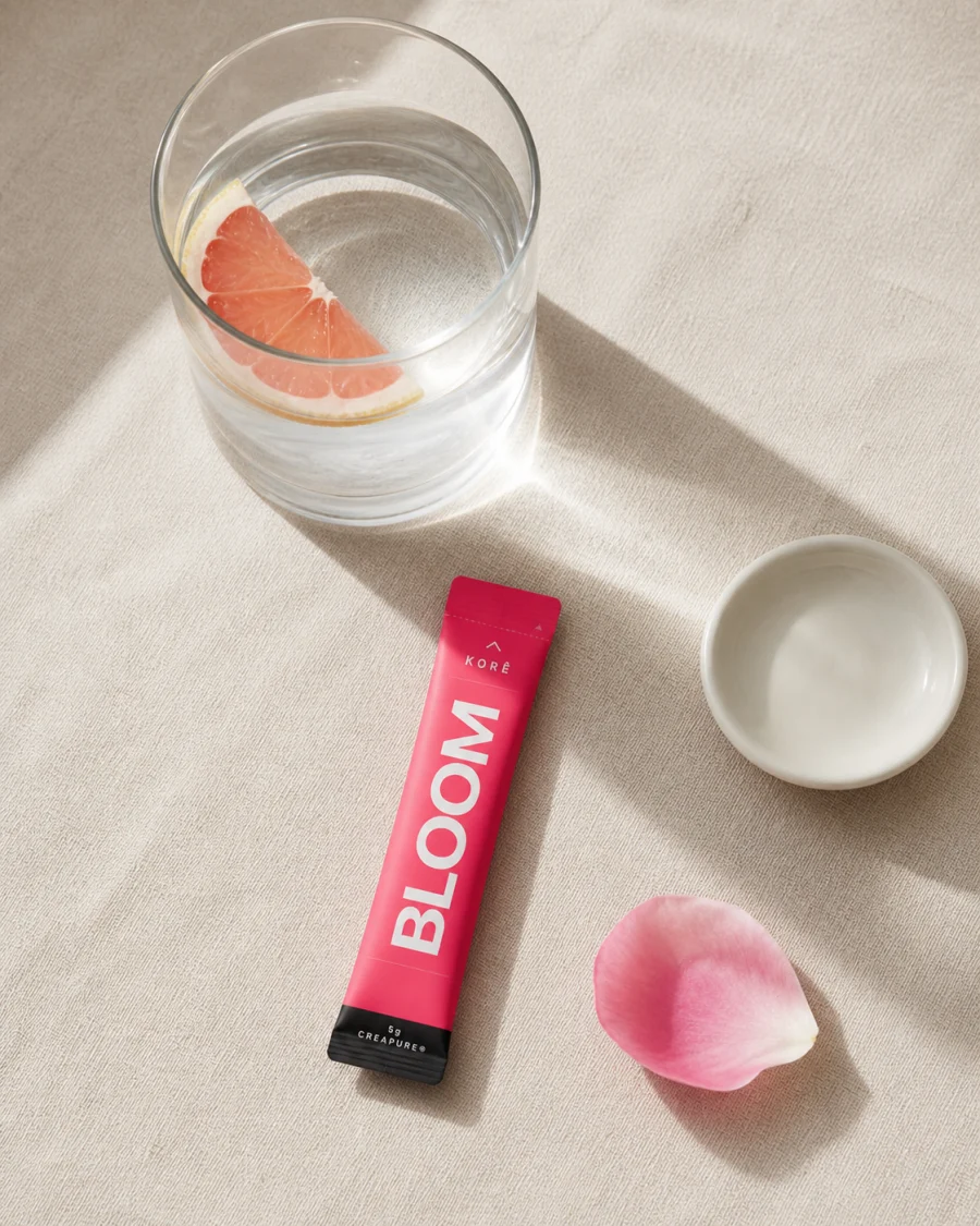 KORÊ BLOOM rose daily stick pack with 5g Creapure creatine monohydrate beside a glass of water